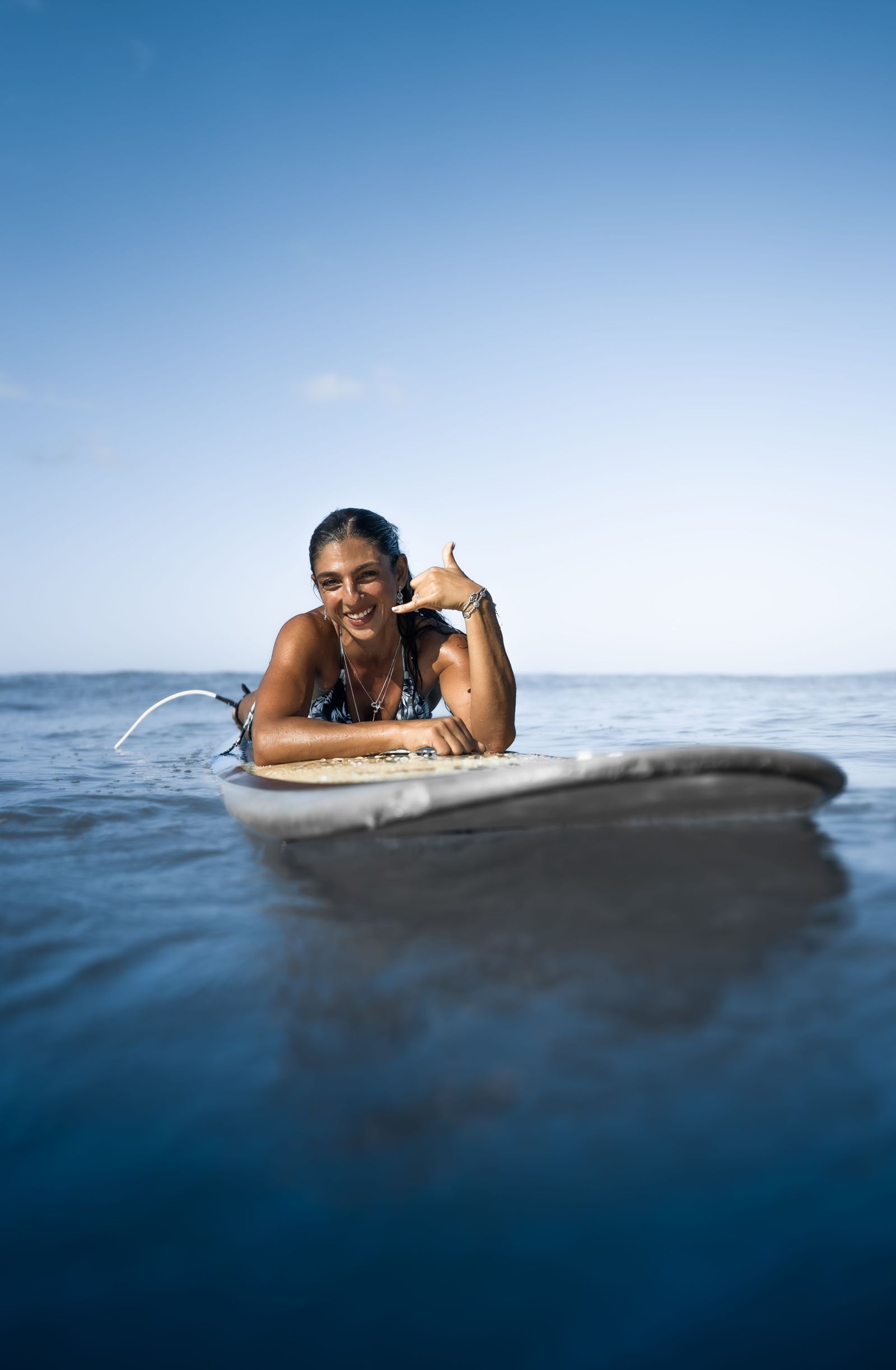 Alumna recostada sobre la tabla en el mar, saludando